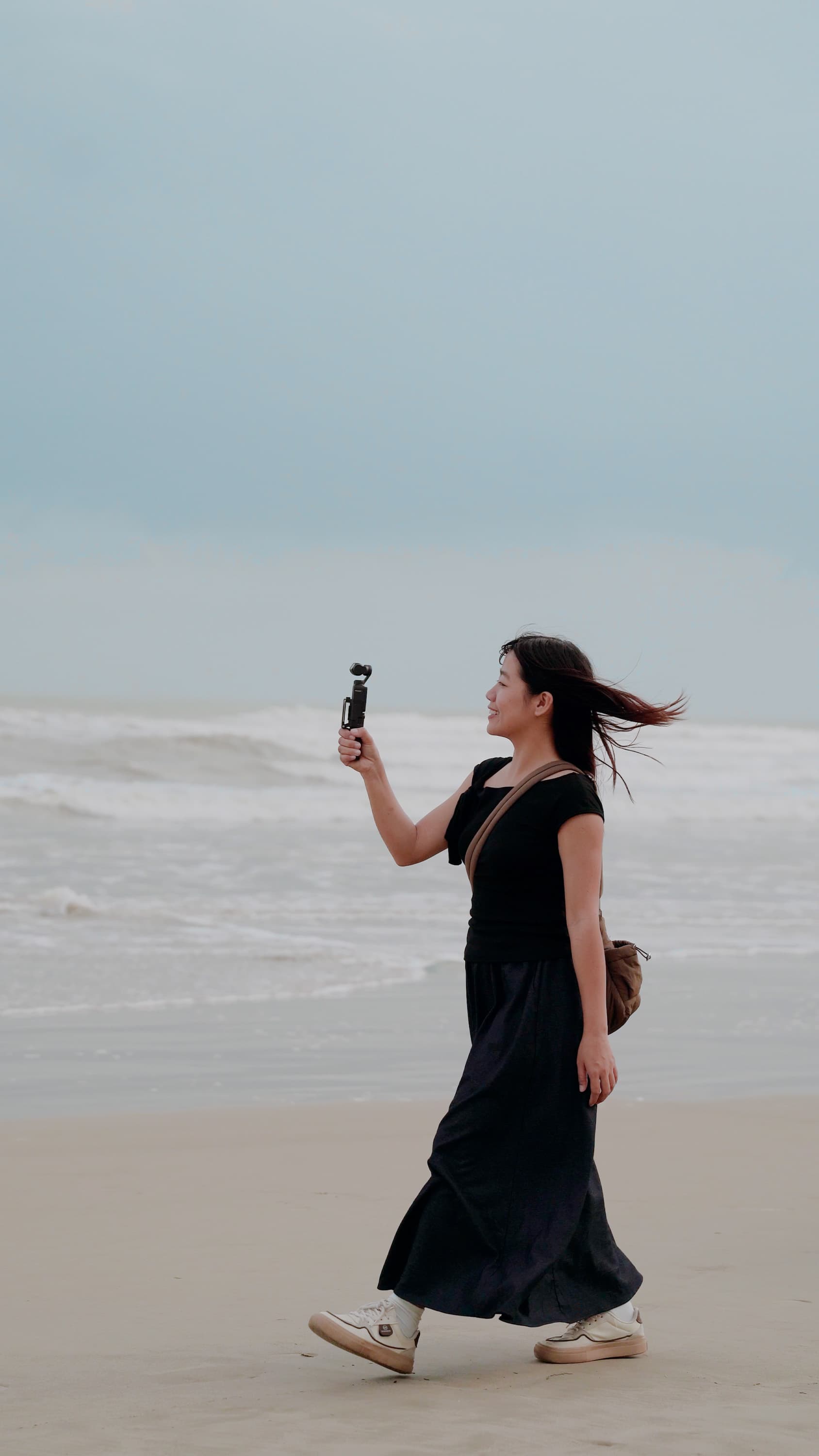 Xuân vừa đi trên bãi biển lộng gió vừa quay video bằng máy quay cầm tay