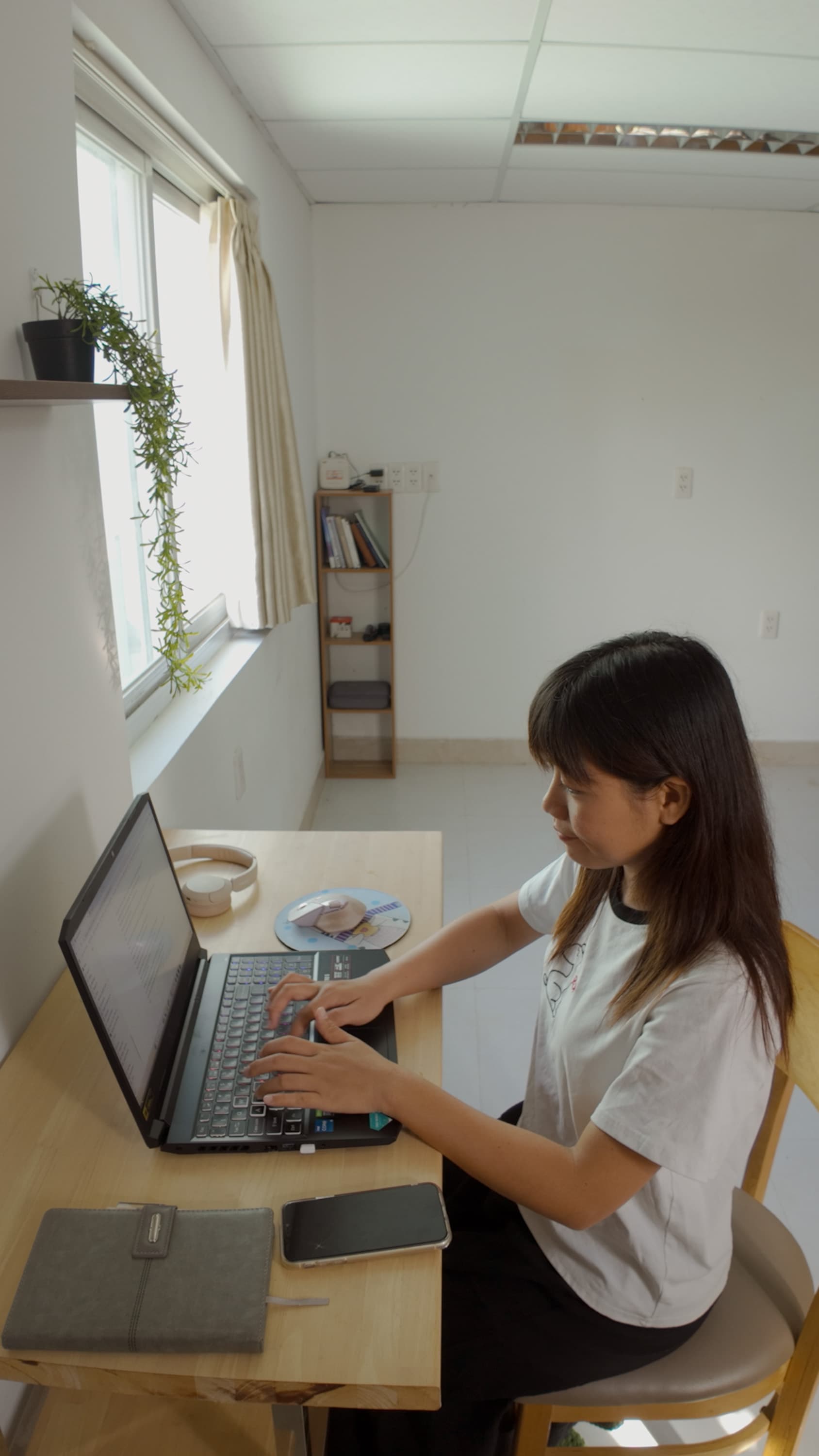 Xuân làm việc bên laptop tại góc bàn cạnh cửa sổ