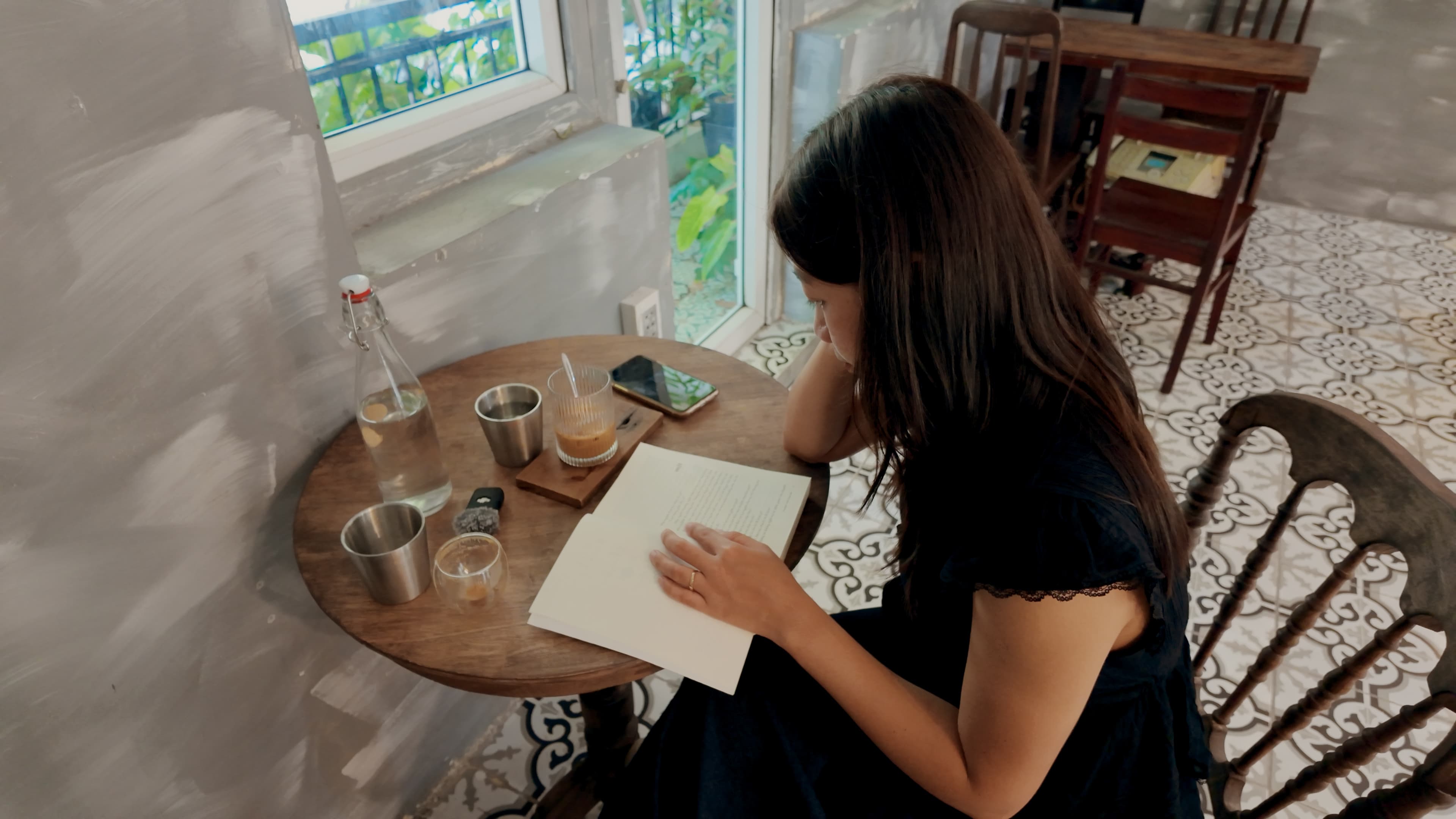 Xuân ngồi đọc tài liệu bên bàn gỗ tròn cạnh cửa sổ quán cà phê
