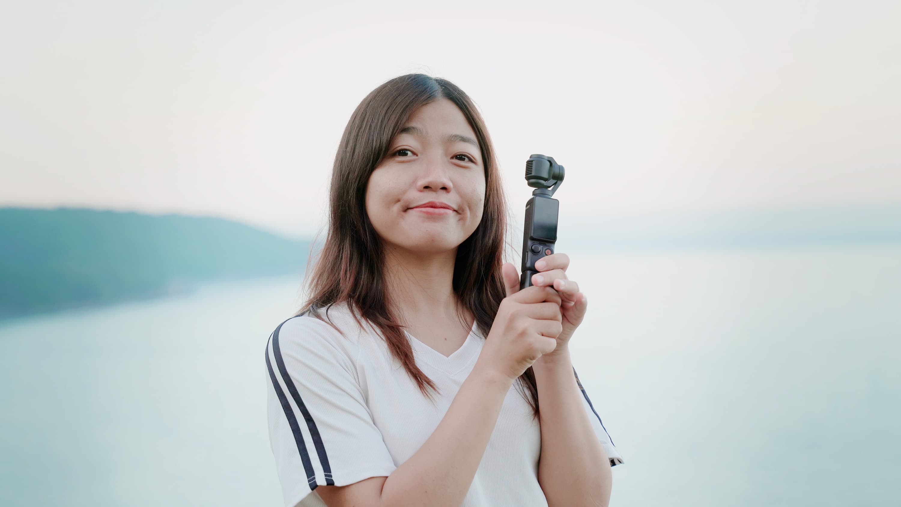 Xuân mỉm cười, cầm chiếc máy quay cầm tay nhỏ gọn bên bờ nước